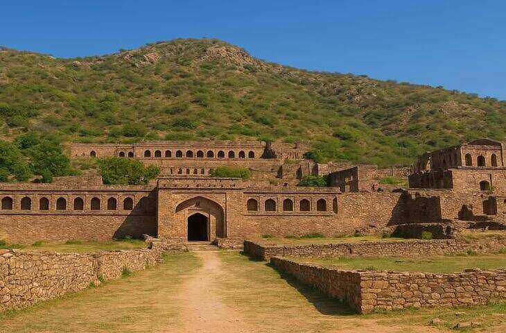 राजस्थान के अलवर जिले में अरावली की पहाड़ियों के बीच स्थित भानगढ़ किला भारत के सबसे चर्चित और रहस्यमयी ऐतिहासिक स्थलों में गिना जाता है। अपनी भव्य वास्तुकला, वीरान गलियों और डरावनी कहानियों के कारण यह किला देश-विदेश के पर्यटकों के आकर्षण का केंद्र बना हुआ है। इसे अक्सर भारत की सबसे डरावनी जगहों में शामिल किया जाता है, हालांकि इसके पीछे इतिहास और लोककथाओं दोनों की भूमिका है।  भानगढ़ किले का इतिहास  भानगढ़ किले का निर्माण 17वीं शताब्दी में हुआ था। इसे आमतौर पर आमेर के राजा भगवान दास के पुत्र माधो सिंह प्रथम से जोड़ा जाता है। यह किला कभी एक समृद्ध नगर हुआ करता था, जहां महल, मंदिर, बाजार और हवेलियां मौजूद थीं। राजस्थान पर्यटन के अनुसार, भानगढ़ कभी एक विकसित बस्ती थी, लेकिन बाद में धीरे-धीरे यहां की आबादी कम होती गई और यह क्षेत्र वीरान हो गया।  किले के परिसर में कई प्राचीन मंदिर, महल और बाजारों के अवशेष आज भी दिखाई देते हैं। यहां प्रवेश के लिए लाहौरी गेट, अजमेरी गेट, फूलबाड़ी गेट और दिल्ली गेट जैसे मुख्य द्वार बने हुए हैं, जो उस समय की स्थापत्य कला की झलक दिखाते हैं।  क्यों कहा जाता है भानगढ़ को रहस्यमयी?  भानगढ़ किले से जुड़ी कई लोककथाएं इसे रहस्यमयी बनाती हैं। सबसे प्रसिद्ध कहानी एक साधु गुरु बालूनाथ और उनके कथित श्राप से जुड़ी है। लोक मान्यता के अनुसार, साधु ने शर्त रखी थी कि किले की ऊंचाई इतनी न बढ़े कि उसकी छाया उनके स्थान तक पहुंचे। बाद में शर्त टूटने पर उन्होंने नगर के विनाश का श्राप दे दिया।  एक अन्य लोकप्रिय कथा तांत्रिक सिंघिया और भानगढ़ की राजकुमारी से जुड़ी है। लोककथा के अनुसार, तांत्रिक राजकुमारी को पाने की कोशिश करता था और असफल होने पर उसने नगर को श्राप दे दिया। हालांकि, इन कहानियों का ऐतिहासिक प्रमाण स्पष्ट रूप से उपलब्ध नहीं है, लेकिन पीढ़ियों से ये कथाएं लोगों के बीच प्रचलित हैं।  रात में प्रवेश पर रोक की चर्चा  भानगढ़ को लेकर सबसे ज्यादा चर्चा इस बात की होती है कि यहां रात में प्रवेश नहीं किया जाता। भारतीय पुरातत्व सर्वेक्षण (ASI) के संरक्षण वाले कई ऐतिहासिक स्थलों की तरह यहां भी निर्धारित समय के बाद प्रवेश प्रतिबंधित रहता है। स्थानीय मान्यताओं और डरावनी कहानियों ने इस प्रतिबंध को और रहस्यमयी बना दिया है।  क्या सच में भूतिया है भानगढ़?  भानगढ़ को लेकर भूत-प्रेत की कहानियां बेहद लोकप्रिय हैं, लेकिन वैज्ञानिक रूप से यहां किसी paranormal गतिविधि की पुष्टि नहीं हुई है। इतिहासकारों के अनुसार, किसी भी प्राचीन नगर के उजड़ने के पीछे युद्ध, राजनीतिक बदलाव, आर्थिक कारण और प्राकृतिक परिस्थितियां अहम भूमिका निभा सकती हैं।  किले की वीरान इमारतें, टूटी दीवारें और सुनसान गलियां लोगों की कल्पना को और बढ़ावा देती हैं। यही कारण है कि इतिहास प्रेमियों के साथ-साथ रोमांच पसंद करने वाले लोग भी यहां बड़ी संख्या में पहुंचते हैं।  भानगढ़ का महत्व  भानगढ़ केवल डरावनी कहानियों के लिए प्रसिद्ध नहीं है, बल्कि यह राजस्थान की समृद्ध विरासत और स्थापत्य कला का महत्वपूर्ण उदाहरण भी है। यह किला हमें उस दौर की सामाजिक, सांस्कृतिक और राजनीतिक स्थिति की झलक देता है।  आज भानगढ़ किला इतिहास, रहस्य और लोककथाओं के अनोखे मेल के रूप में जाना जाता है। इसकी पत्थरों में छिपी कहानियां इसे भारत के सबसे अलग और आकर्षक ऐतिहासिक स्थलों में शामिल करती हैं।