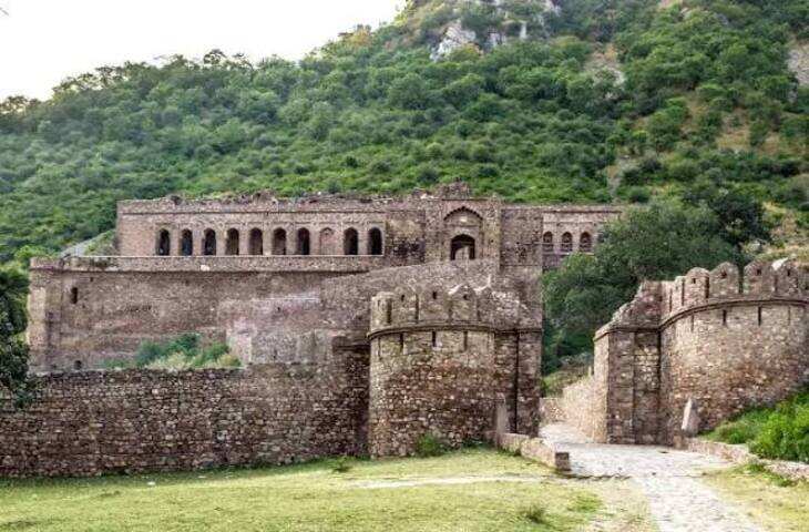 राजस्थान के अलवर जिले में अरावली की पहाड़ियों के बीच स्थित भानगढ़ किला इतिहास, वास्तुकला और रहस्यमयी कहानियों का अनोखा संगम है। कभी रौनक से भरा यह इलाका आज खंडहरों में तब्दील हो चुका है। सुनसान महल, पुराने मंदिर, वीरान बाजार और ऊंची किलेबंदी भानगढ़ के पुराने वैभव की कहानी कहते हैं। यही वीरानी और इससे जुड़ी लोककथाएं इसे देश के सबसे चर्चित कथित 'भूतिया' स्थानों में शामिल करती हैं।  कभी 9 हजार से ज्यादा घरों की थी बस्ती  भानगढ़ को केवल एक किले के रूप में देखना सही नहीं होगा। यह कभी एक पूरी आबाद नगरी थी। राजस्थान पर्यटन के मुताबिक यहां 9 हजार से ज्यादा मकान होने का उल्लेख मिलता है। किले के भीतर महल, हवेलियां, मंदिर और बाजार मौजूद थे। तीन स्तर की किलेबंदी और पांच विशाल द्वार इस नगर की सुरक्षा व्यवस्था का हिस्सा थे।  किले में आज भी गोपीनाथ मंदिर, सोमेश्वर मंदिर, केशव राय मंदिर, मंगला देवी मंदिर और गणेश मंदिर के अवशेष देखे जा सकते हैं। राजमहल के बारे में कहा जाता है कि वह कभी सात मंजिला था, हालांकि अब इसकी केवल कुछ मंजिलें ही बची हैं।  बाबा बालू नाथ के श्राप की कहानी  भानगढ़ से जुड़ी सबसे प्रसिद्ध कहानियों में एक बाबा बालू नाथ की है। स्थानीय मान्यता के अनुसार, किला और नगर बसाने से पहले साधु से अनुमति ली गई थी। शर्त थी कि यहां बनने वाली किसी भी इमारत की छाया उनके निवास पर नहीं पड़नी चाहिए।  कहानी के मुताबिक बाद में किले की ऊंचाई बढ़ाई गई और उसकी छाया साधु के स्थान तक पहुंच गई। इसके बाद उन्होंने नगर के विनाश का श्राप दे दिया। हालांकि, यह कथा लोकमान्यता है, इसका ऐतिहासिक प्रमाण नहीं मिला है।  राजकुमारी रत्नावती और तांत्रिक की कहानी  भानगढ़ की दूसरी चर्चित कहानी राजकुमारी रत्नावती और एक तांत्रिक से जुड़ी है। लोककथा के अनुसार, तांत्रिक राजकुमारी पर मोहित था और उसने कथित तौर पर जादू के जरिए उन्हें अपने वश में करने की कोशिश की।  राजकुमारी को जब इसकी जानकारी हुई तो कथित रूप से उसने तांत्रिक की चाल नाकाम कर दी। कहानी में बताया जाता है कि मृत्यु से पहले तांत्रिक ने भानगढ़ को श्राप दिया। बाद में नगर उजड़ गया और लोगों ने इस घटना को किले के रहस्य से जोड़ दिया। यह कहानी भी लोककथा के रूप में प्रचलित है, प्रमाणित इतिहास नहीं।  सूर्यास्त के बाद प्रवेश क्यों नहीं?  भानगढ़ की रहस्यमयी पहचान का सबसे बड़ा कारण यहां सूर्यास्त के बाद प्रवेश पर प्रतिबंध है। राजस्थान पर्यटन के अनुसार किले में सूर्योदय से पहले और सूर्यास्त के बाद प्रवेश की अनुमति नहीं है। यही नियम इस स्थान से जुड़ी डरावनी कहानियों को और हवा देता है।  हालांकि, इस प्रतिबंध को भूत-प्रेत की मौजूदगी का प्रमाण मानना सही नहीं होगा। किला खंडहरों में है और कई संरचनाएं पुरानी तथा असुरक्षित हैं। रात में अंधेरा और दुर्गम इलाका पर्यटकों के लिए जोखिम बढ़ा सकता है।  क्या सच में भानगढ़ भूतिया है?  भानगढ़ को 'भारत की सबसे भूतिया जगह' कहे जाने के पीछे मुख्य आधार लोककथाएं, लोगों की धारणाएं और इसकी वीरान संरचनाएं हैं। किसी अलौकिक घटना का वैज्ञानिक प्रमाण उपलब्ध नहीं है। राजस्थान पर्यटन भी इसे रहस्यमयी और कथित रूप से प्रेतबाधित स्थान के तौर पर प्रस्तुत करता है, लेकिन इसके साथ जुड़ी कहानियों को किंवदंतियों के रूप में ही बताया जाता है।  इसलिए भानगढ़ की असली खूबसूरती शायद उसके कथित भूतों में नहीं, बल्कि उसके सदियों पुराने इतिहास, मंदिरों, राजमहल और अरावली की प्राकृतिक पृष्ठभूमि में छिपी है। इतिहास और रहस्य का यही मेल हर साल बड़ी संख्या में पर्यटकों को यहां खींचता है।